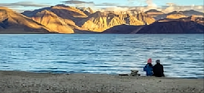 Couple sitting by Pangong Lake with mountains in Ladakh