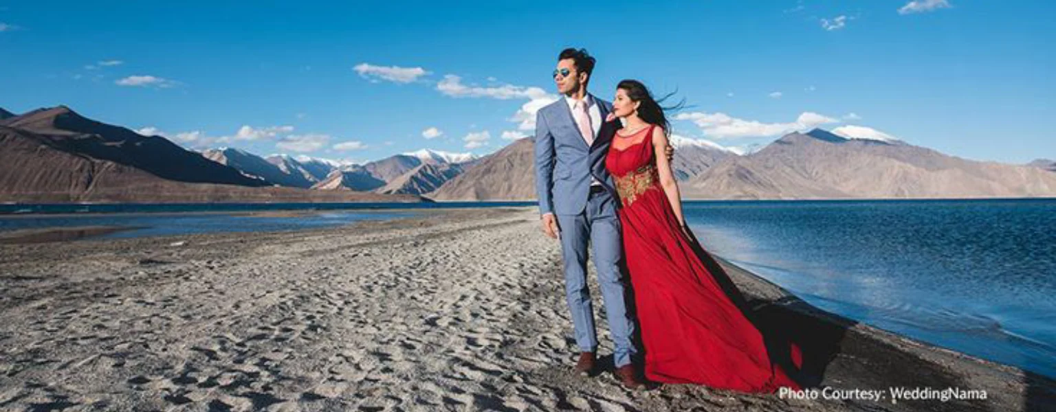Couple posing by Pangong Lake in Ladakh with mountains and blue sky background triphills.com
