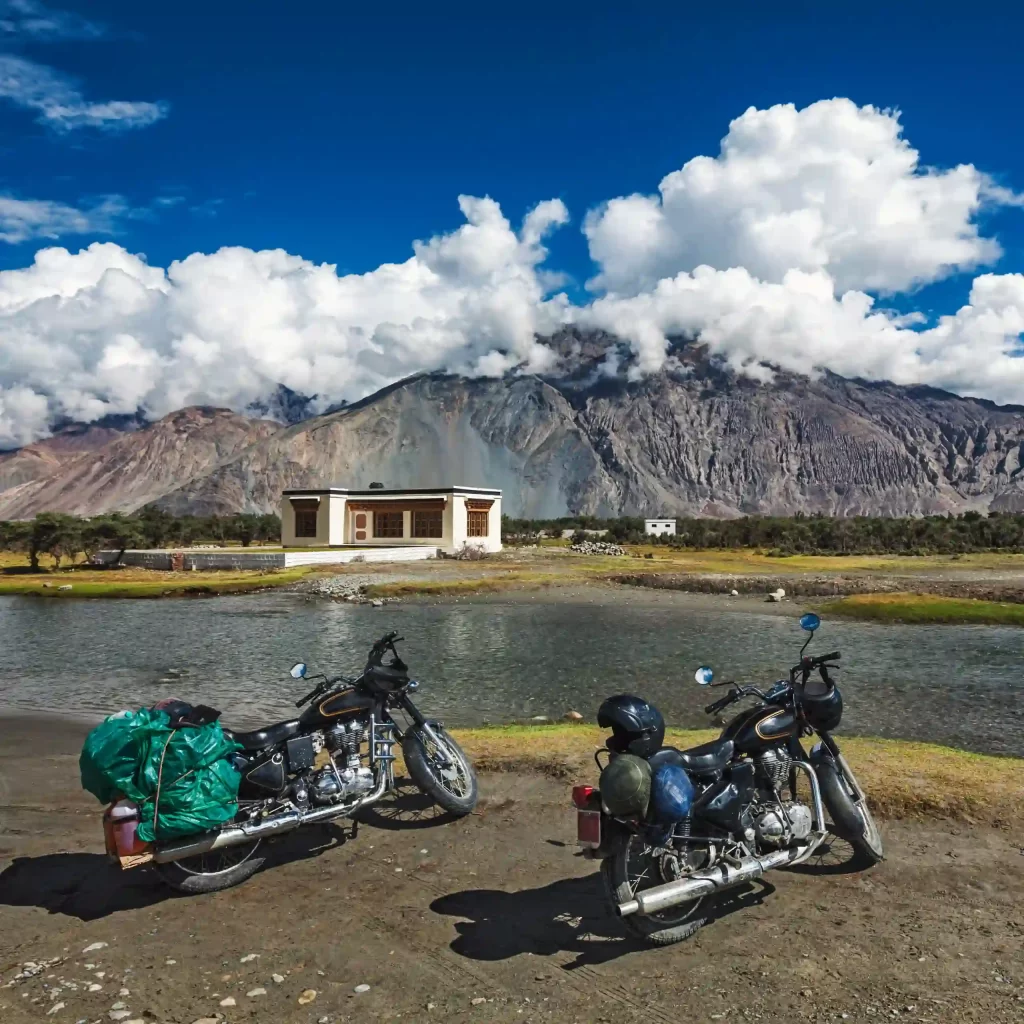 Motorcycles parked beside a river in Ladakh with mountains in the background.