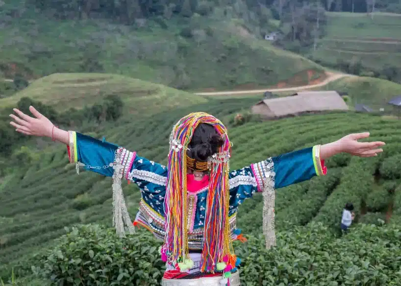 Person in traditional attire overlooking lush green tea gardens with open arms.